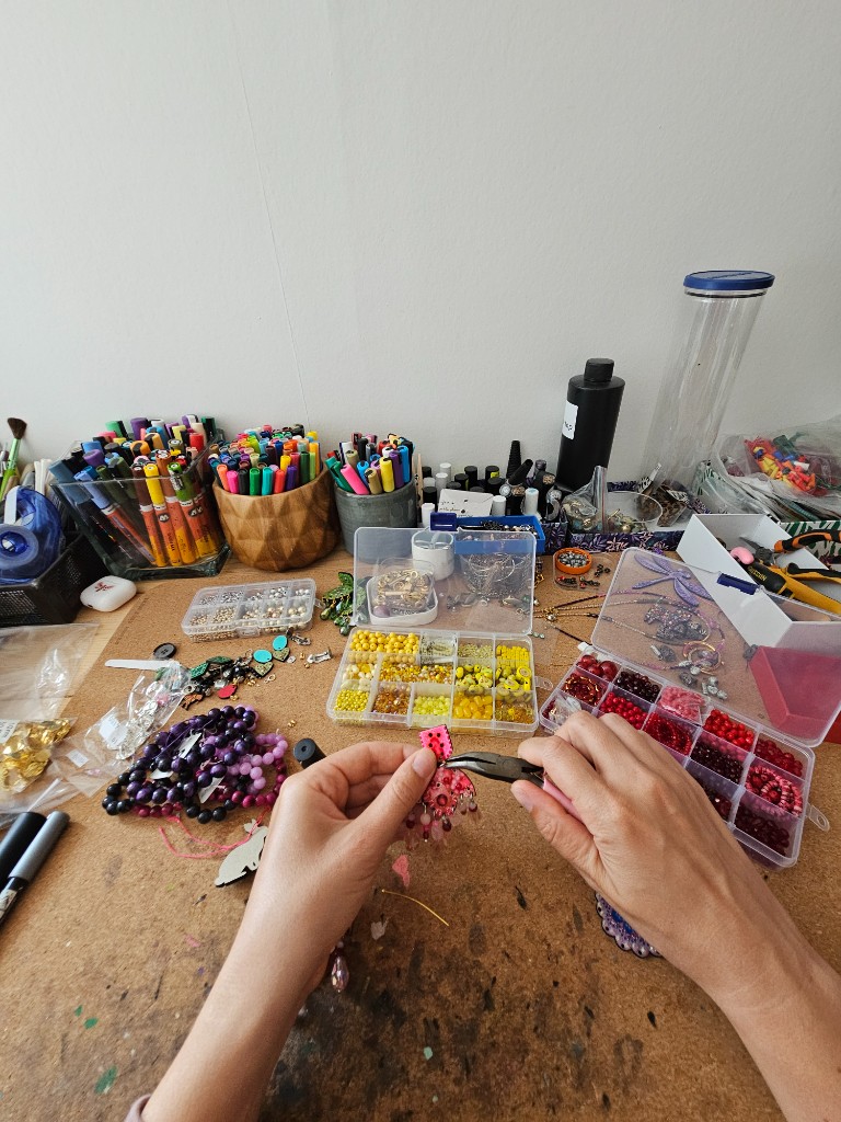 Mains d’Alis assemblant une paire de boucles d’oreilles dans l’atelier